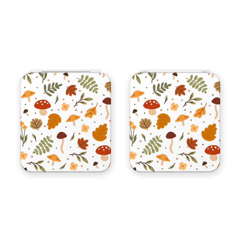 Two square coasters with white backgrounds, featuring a whimsical autumn-themed pattern. The design includes mushrooms, fern leaves, various plant elements, and scattered fall-colored leaves in shades of orange, brown, and green. Perfect for adding charm to your table while you play Nintendo Switch with the Cozy Autumn Game Card Box by petimint.