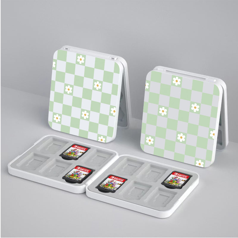 Introducing the Checkered Flowers Game Card Box for Nintendo Switch by petimint. This set includes two open white cases adorned with charming green and white checkered patterns, accented by delicate white flowers. Each box features two slots: one slot securely holds two Nintendo Switch game cards with distinct red labels and unique cover art, while the other slot remains empty for additional storage. A perfect addition to any cozygamer's collection.