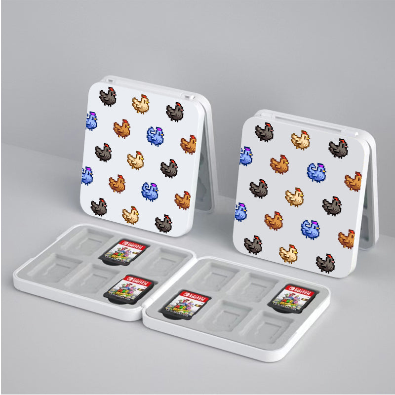 Two white, square "Chicken Stardew Valley Game Card Box for Nintendo Switch" cases by petimint are adorned with colorful pixelated birds in shades of brown, blue, orange, and black. They stand open on a gray surface. In front of them lie two cases with several slots each, holding Nintendo Switch game cartridges—every cozygamer's dream setup—with two games visible.
