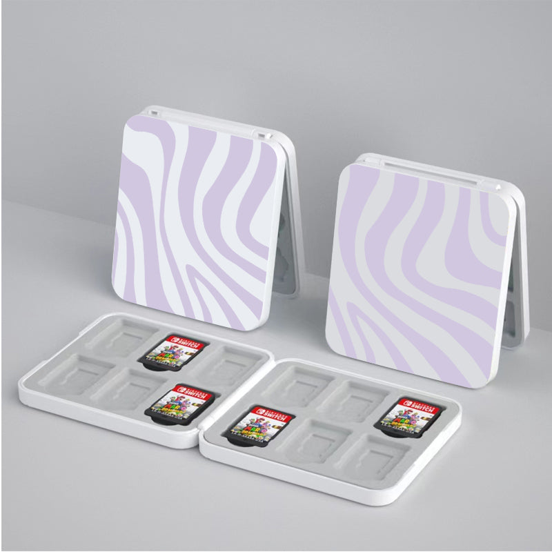 Two square, pastel lavender-and-white, zebra-patterned petimint Zebra Game Card Boxes for Nintendo Switch are open, revealing compartments designed to hold game cartridges. Each box has space for six cartridges, with some of the slots occupied by Nintendo Switch game cards—a perfect accessory for any cozy gamer.