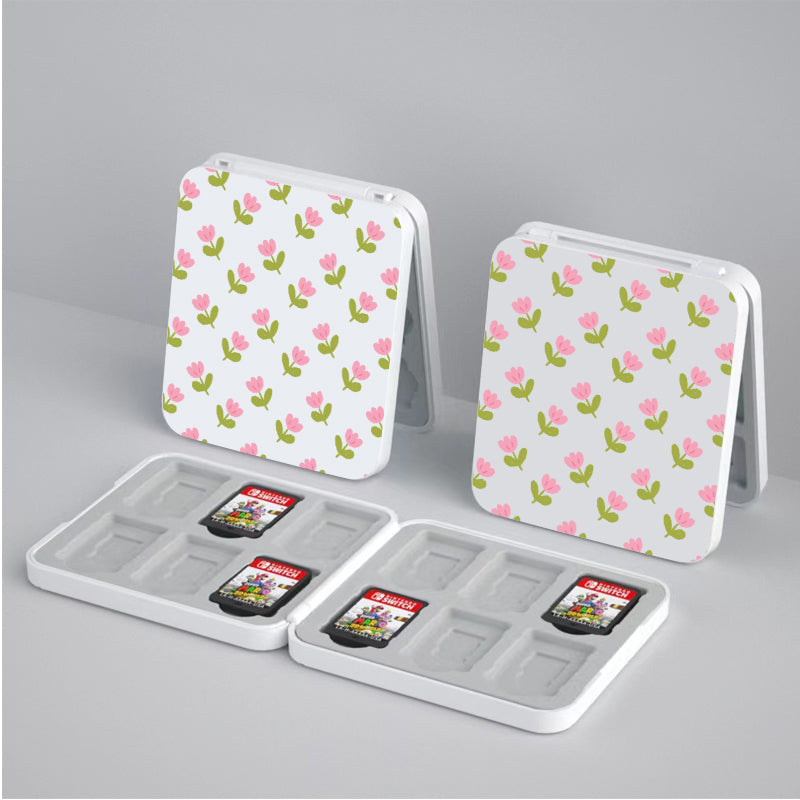 Two Pink Tulips Game Card Boxes for Nintendo Switch by petimint are open to reveal compartments holding game cartridges. Perfect for the cozy gamer, these white, square storage cases feature pink and green flower designs with floral patterns on the exterior and are displayed on a light gray surface.