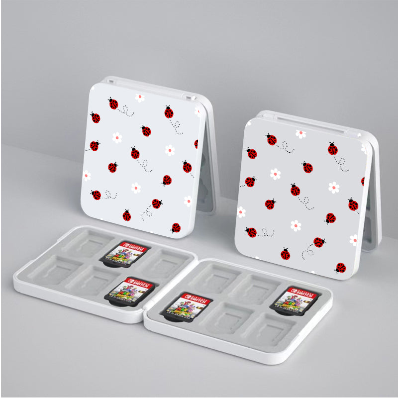 Two white, rectangular petimint Little Ladybug Game Card Boxes for Nintendo Switch are open, revealing storage compartments for SD cards inside. Two SD cards are shown in the compartments, each showcasing a different game for the Nintendo Switch. The cozygamer setup rests on a light-colored surface.