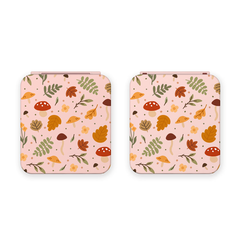 Two square-shaped items with a beige background and a colorful autumn-themed pattern, possibly Cozy Autumn Game Card Boxes for Nintendo Switch by petimint. The pattern includes illustrations of orange and yellow leaves, mushrooms, acorns, and small foliage against a pink color scheme.