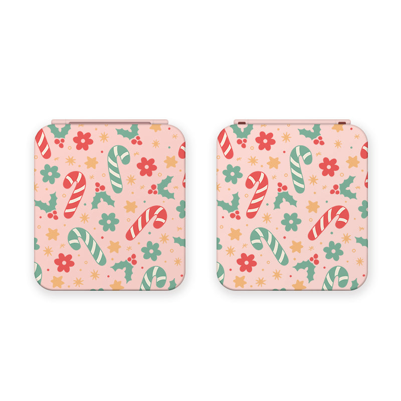 Two pink Candy Cane Game Card Boxes for the Nintendo Switch by petimint, each featuring a festive pattern of red, green, and white candy canes, flowers, stars, and holly leaves. Perfect for a cozy gamer's setup right next to the console.