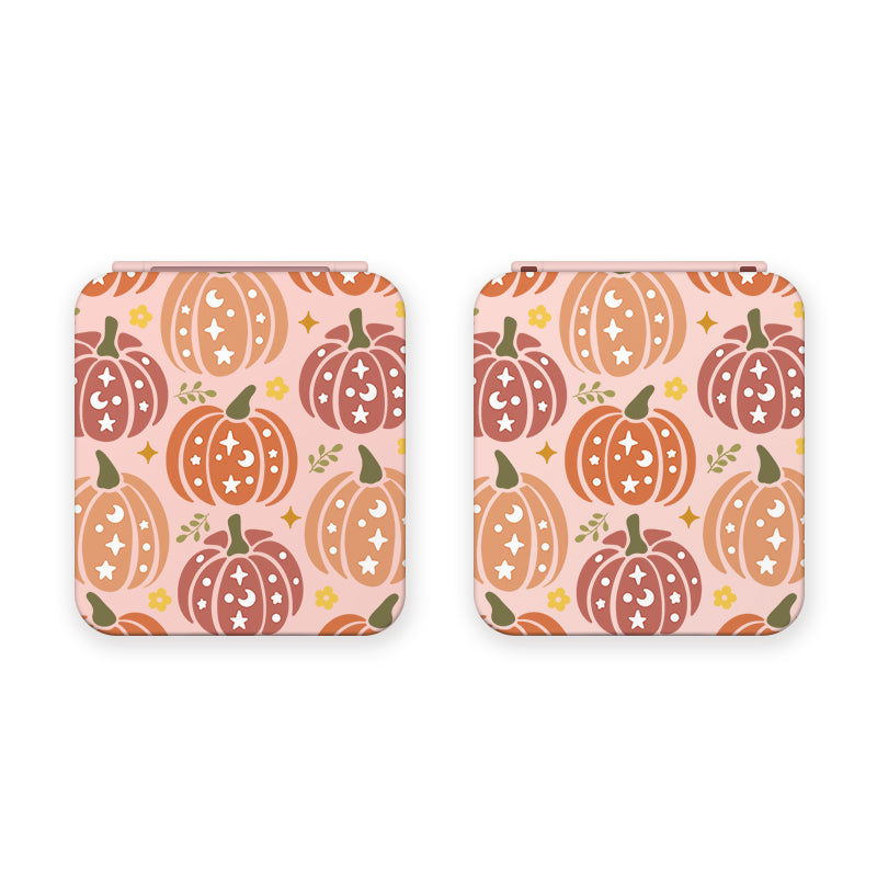 Two square-shaped Pumpkins Game Card Boxes by petimint feature a pattern of colorful pumpkins on a light background. The pumpkins, reminiscent of quirky gamer artwork, are decorated with stars and moons in shades of orange, red, and brown, complemented by scattered green leaves and small yellow flowers. The color of the boxes is pink.