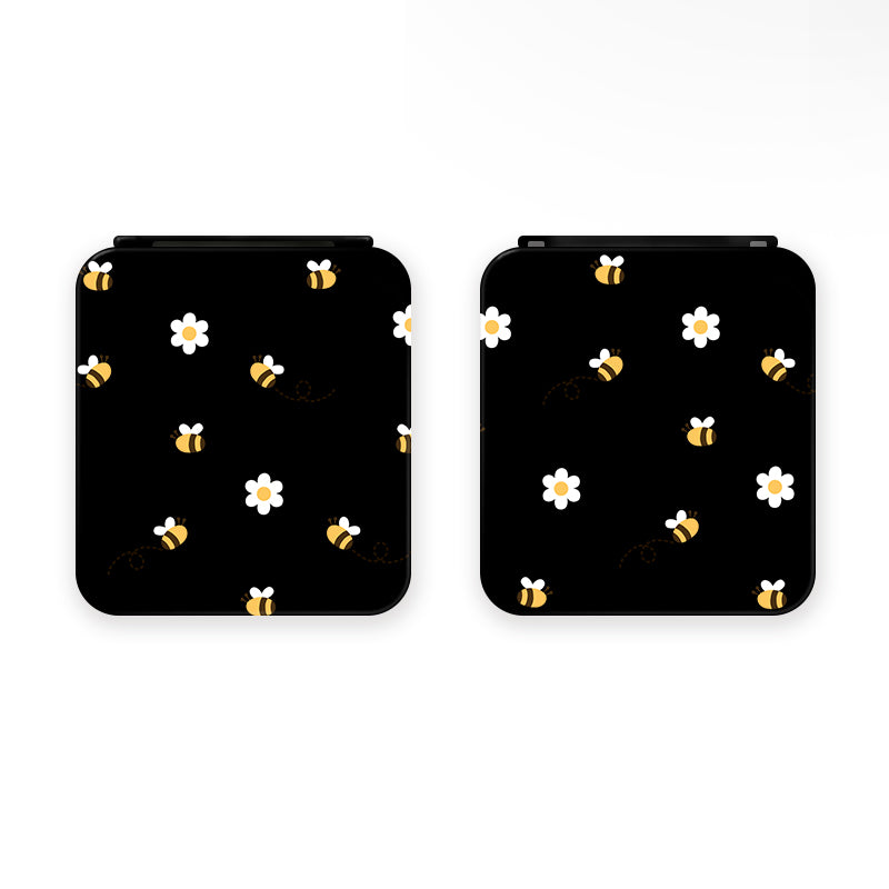 Two square-shaped black "Little Bee Game Card Box for Nintendo Switch" devices by petimint, perfect for cozygamer enthusiasts, feature a playful design of yellow bees and white flowers scattered across their surface. The devices are positioned side by side against a white background.