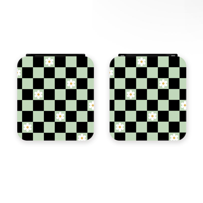 Two Checkered Flowers Game Card Boxes for the Nintendo Switch by petimint, featuring a black and light green checkerboard pattern adorned with small white flowers with yellow centers. The checkerboard design covers the entire surface of each box, making them the perfect cozygamer accessory. The background is plain white.