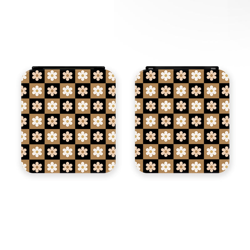 The Cozy Checkered Flowers Game Card Box for Nintendo Switch by petimint is ideal for any Nintendo Switch enthusiast. This black square card box features a striking checkerboard pattern with alternating black and white squares, each adorned with a beige flower at the center of the white squares. The edges are rounded, and the boxes are displayed side by side against a light background.