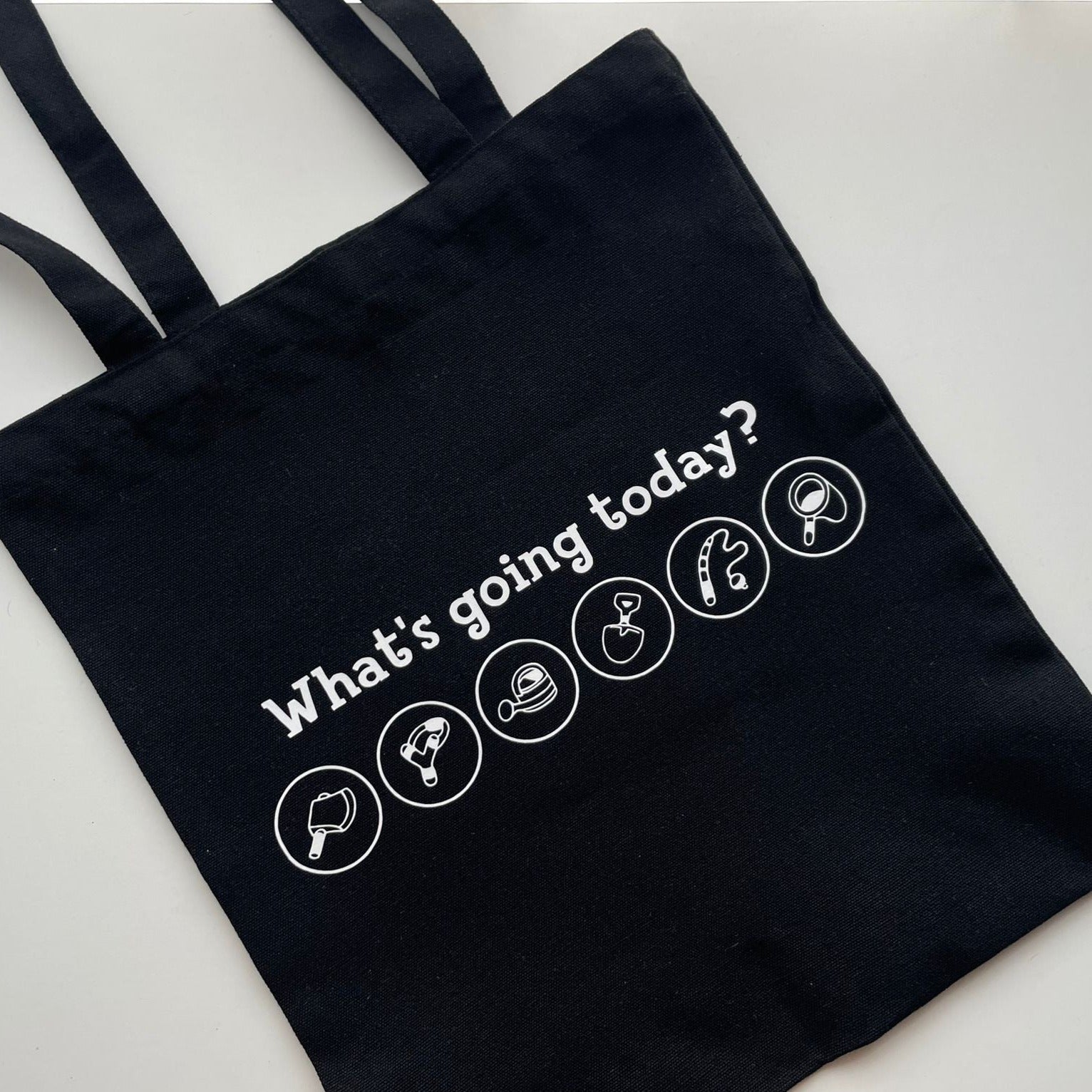 The Animal Crossing Tools Tote Bag by petimint is a black tote bag featuring the phrase "What's going today?" printed in white. Below the text, you'll find five white circular icons depicting a coffee cup, a hairdryer, a shower head, a makeup brush, and a Nintendo Switch—perfect for any cozygamer on the go.