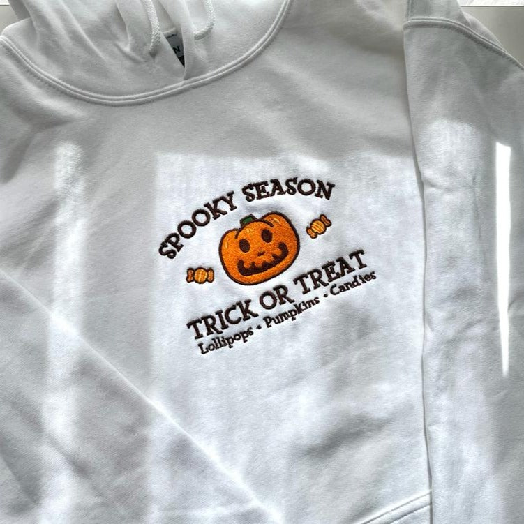 Introducing the Jack Spooky Season Hoodie by petimint! This white hoodie showcases a vibrant Halloween-themed design, ideal for gamers. It features a central smiling jack-o'-lantern flanked by candy corn, with "Spooky Season" written above and "Trick or Treat" followed by "Lollipops • Pumpkins • Candies" below.