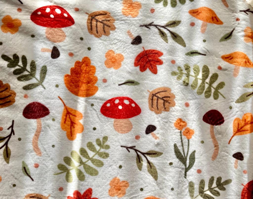 Discover the Cozy Autumn Soft Blanket by petimint – a perfect addition to your home decor. This whimsical autumn-themed blanket features a charming pattern of red and brown mushrooms, vibrant orange and red leaves, lush green fern leaves, and delicate flowers scattered across a pristine white background. It's ideal for creating a cozy atmosphere that adds charm to any room.