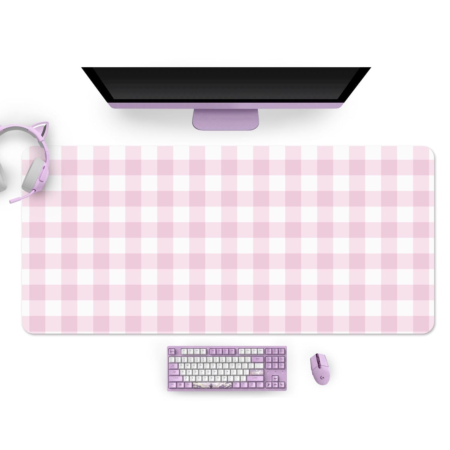 A cozy gamer setup featuring a monitor, a petimint Picnic Mouse Pad in pink covering the desk, a purple keyboard, a matching purple mouse, and a pair of purple cat-ear headphones resting on the left side of the desk.