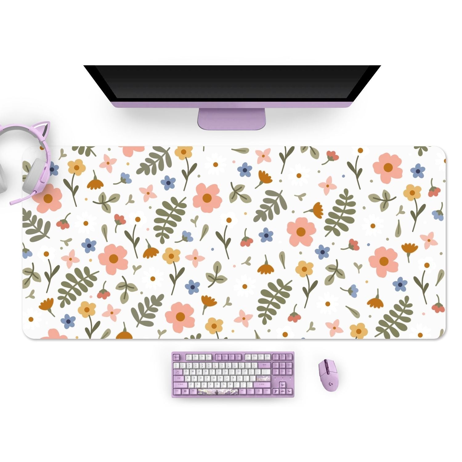 A pastel purple gamer setup featuring a monitor, keyboard, mouse, and cat-ear headphones. The desk mat is the "Spring Mouse Pads PC Gaming Accessories" by petimint, decorated with a floral pattern in shades of pink, blue, orange, and green on a white background. A Nintendo Switch sits beside the setup for ultimate gaming versatility.