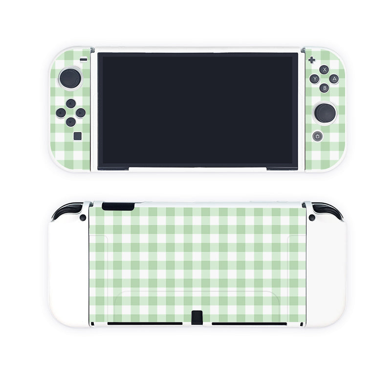 A gaming console, equipped with petimint's Picnic Case for Nintendo Switch, is shown in two views: front and back. The front features a blank screen with white Joy-Con controllers on either side, adorned with a light green and white checkered pattern. The back of this Nintendo Switch showcases the same charming green checkered pattern across the entire surface.