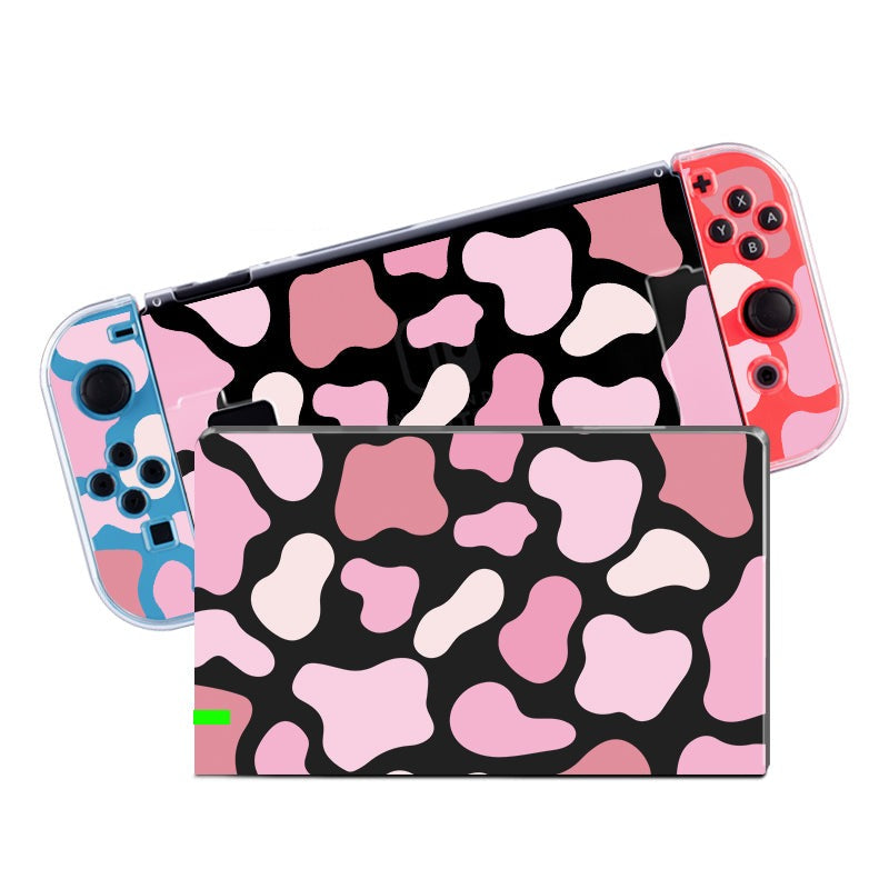 Introducing the Strawberry Cow Case for Nintendo Switch by petimint: a gaming console featuring a vibrant mix of pink, black, and cream in an abstract pattern. It includes controllers with transparent cases—one in blue and the other in red. A soft TPU switch grip case provides comfort while preserving the design's unique overlapping, irregular shape motif.