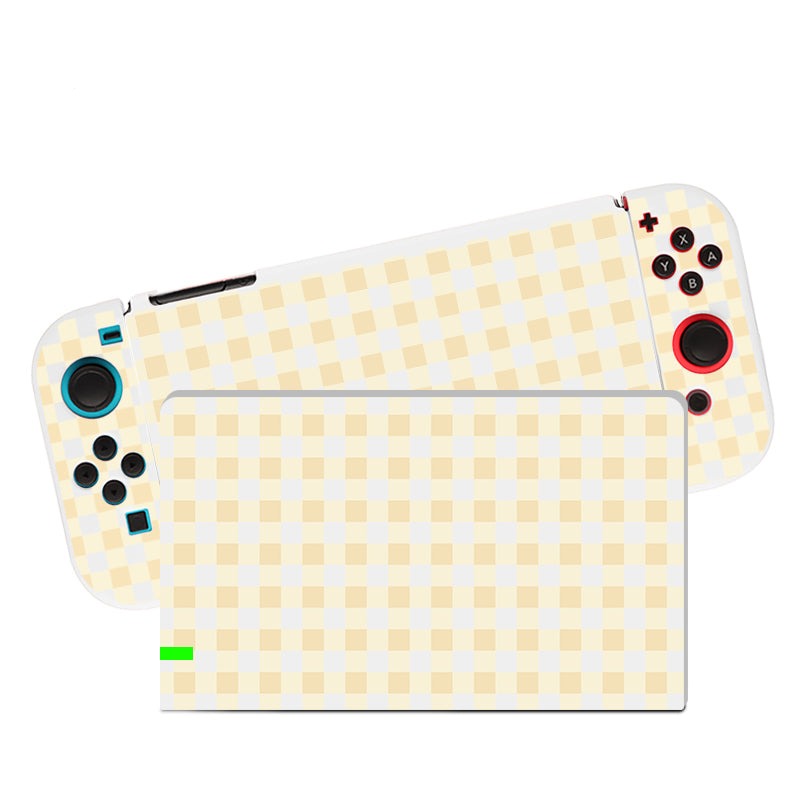 The Picnic Case for Nintendo Switch by petimint is showcased as a handheld gaming console with removable controllers. The device and its controllers boast a beige and cream checkered pattern design, with the left controller highlighted in blue and the right controller accented in red around the buttons. All of this is encased in a soft yellow TPU dockable case for added protection.