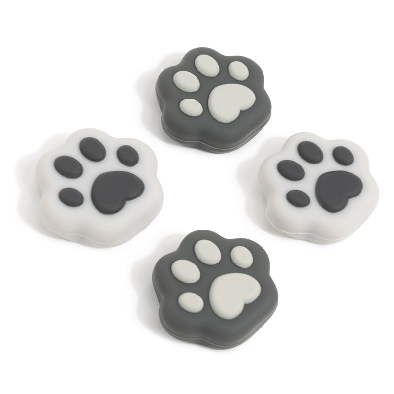 Four petimint Grey Cat Paw Thumb Grips for Nintendo Switch, designed for enthusiasts, are displayed in a square formation. Two grips feature a dark gray base with light gray pads, while the other two have a white base with dark gray pads, creating a whimsical and balanced pattern reminiscent of paw-shaped silicone coasters.