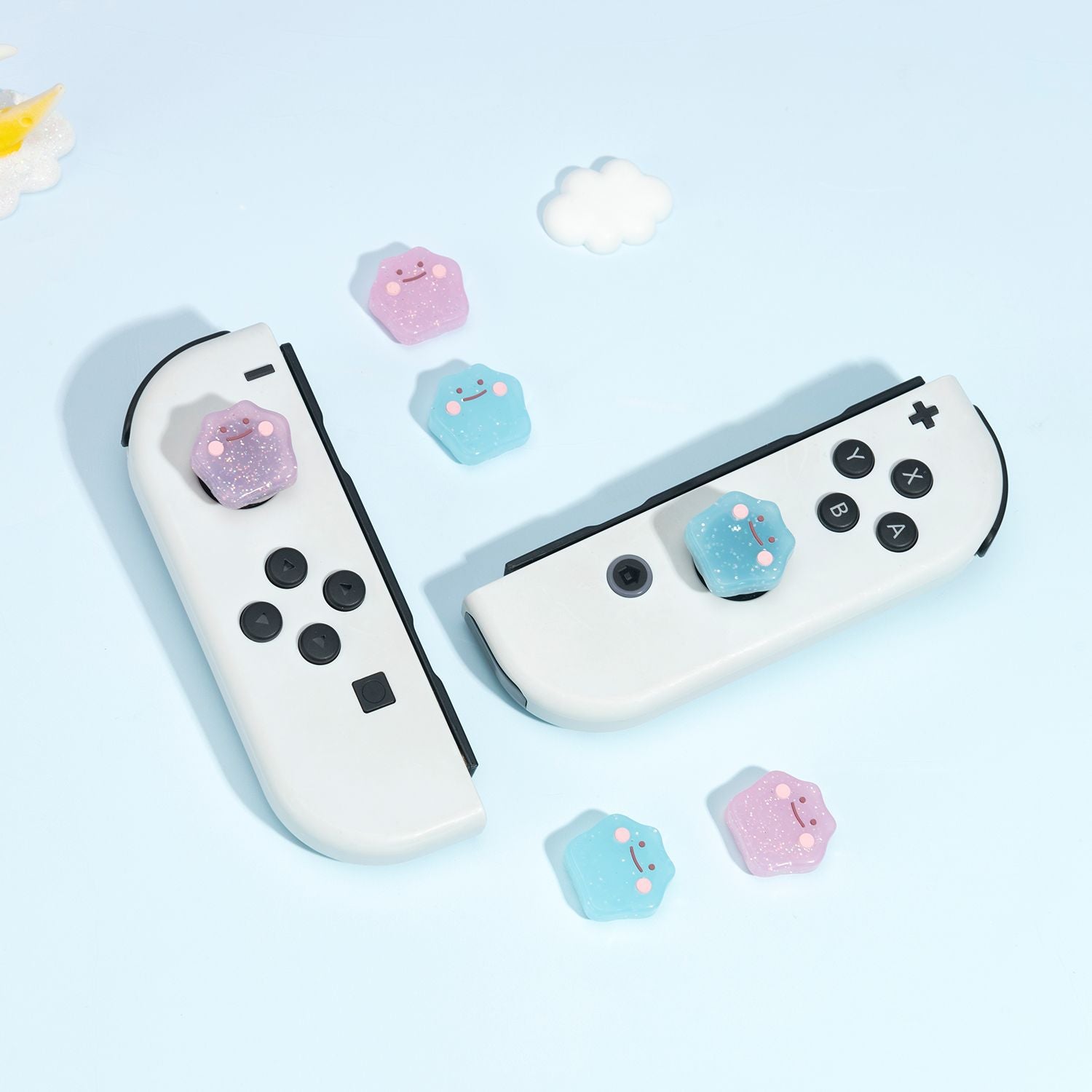 Two white gaming controllers with black buttons sport colorful, hexagonal keycaps in pink and blue, perfectly complemented by the petimint Glitter Ditto Thumb Grips for Nintendo Switch. Additional keycaps and a small cloud decoration surround the controllers on a light blue background.