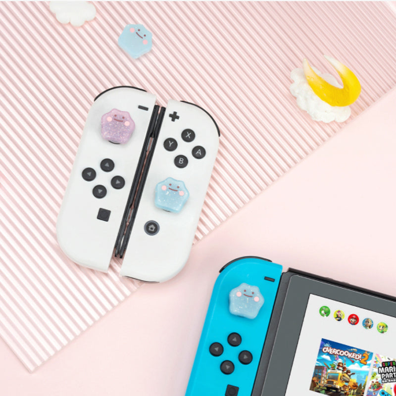 A Nintendo Switch featuring removable Joy-Con controllers enhanced with charming petimint Glitter Ditto Thumb Grips shaped like cats. The console's screen showcases game icons set against a background of striped and solid pink, beautifully adorned with decorative clouds and a moon.