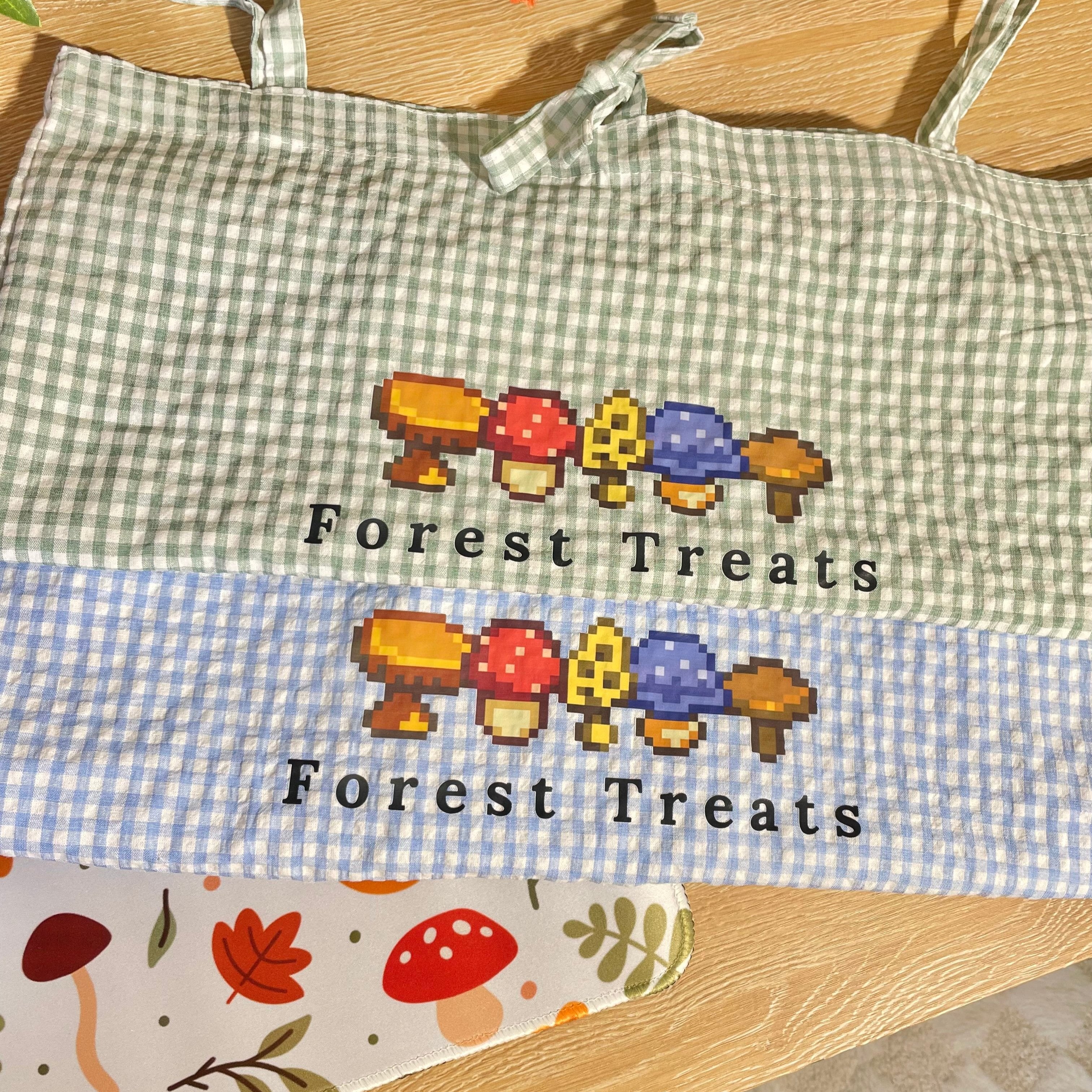 Introducing the Forest Treats Picnic Tote Bag by petimint! This charming tote features a green and white checkered pattern on the top half and a blue and white checkered pattern on the bottom half. Perfect for any cozygamer, it showcases pixel art images of colorful mushrooms with "Forest Treats" printed below them.