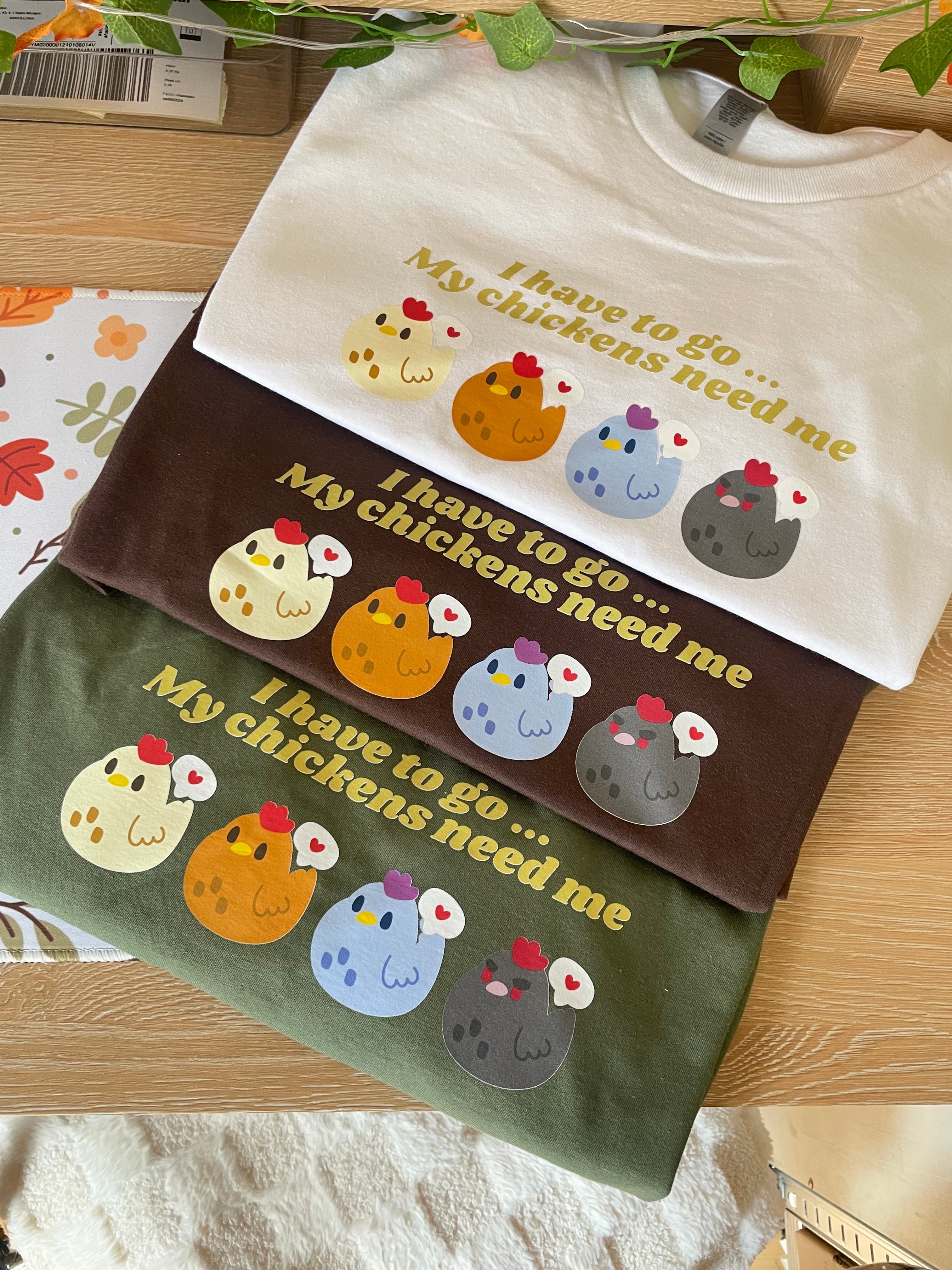 Three folded My Chickens Need Me T-Shirts by petimint in white, brown, and green each display the phrase 