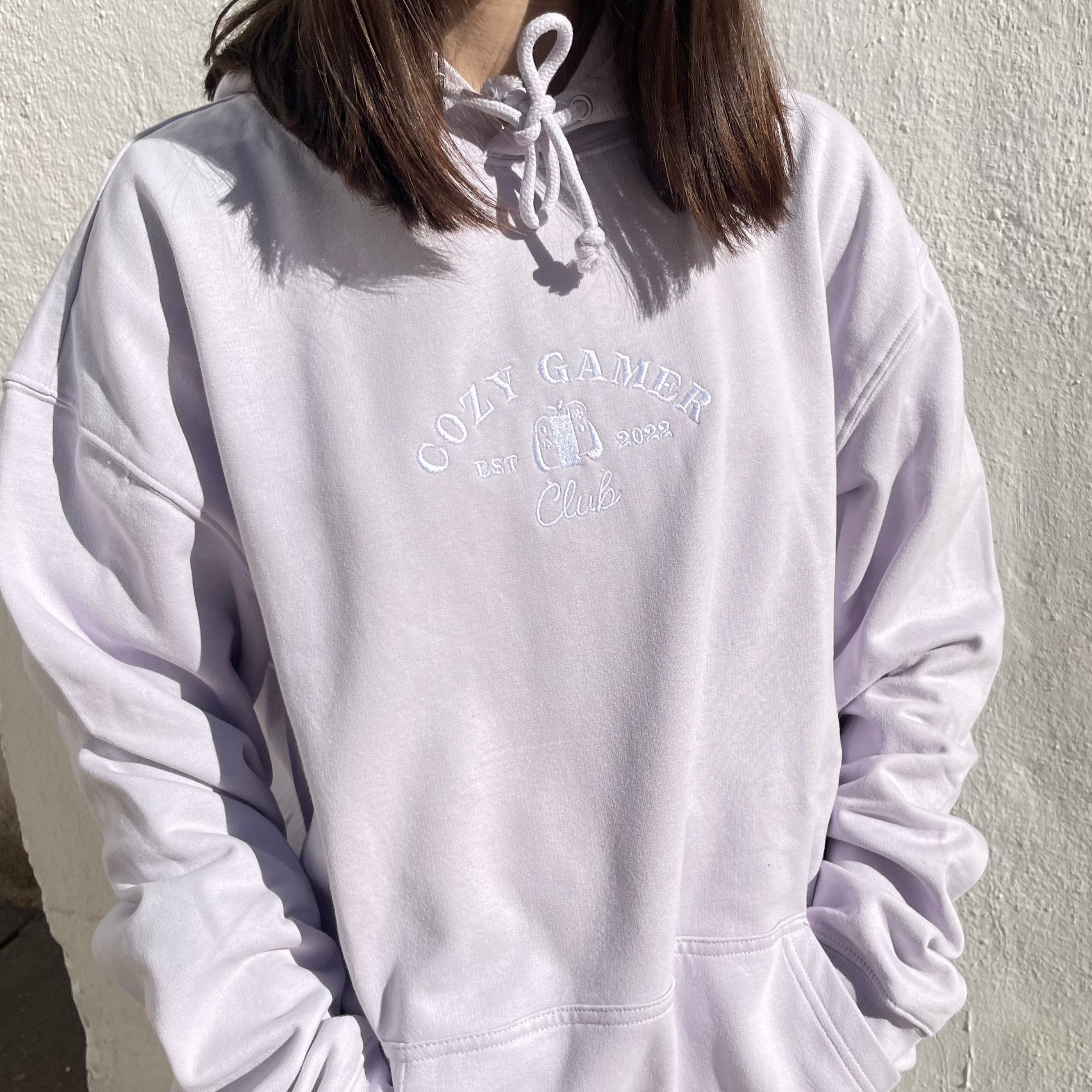 A person in a pastel lilac Cozy Gamer Club Hoodie by petimint, with 