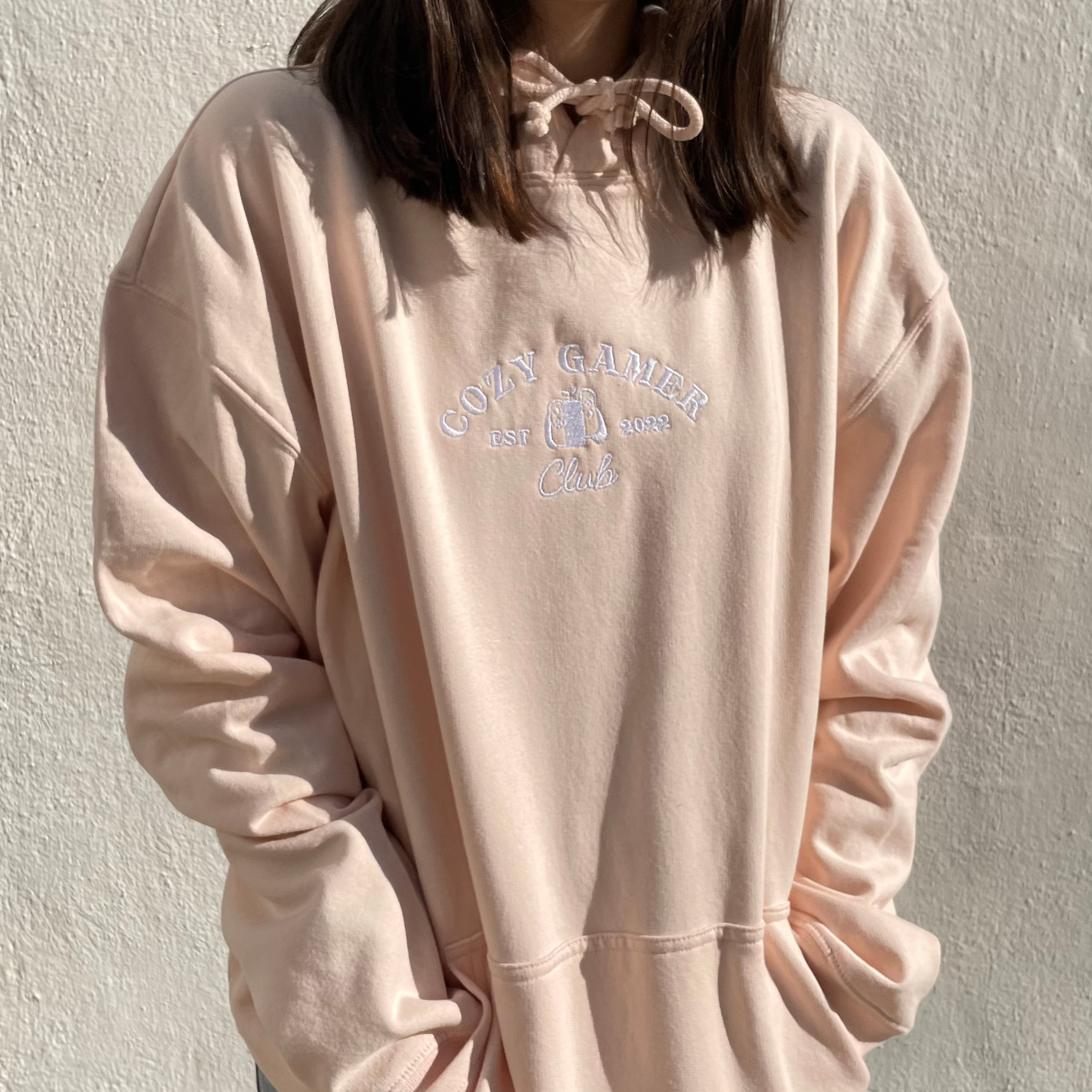 A person is dressed in a light pink, 100% cotton Cozy Gamer Club Hoodie with 