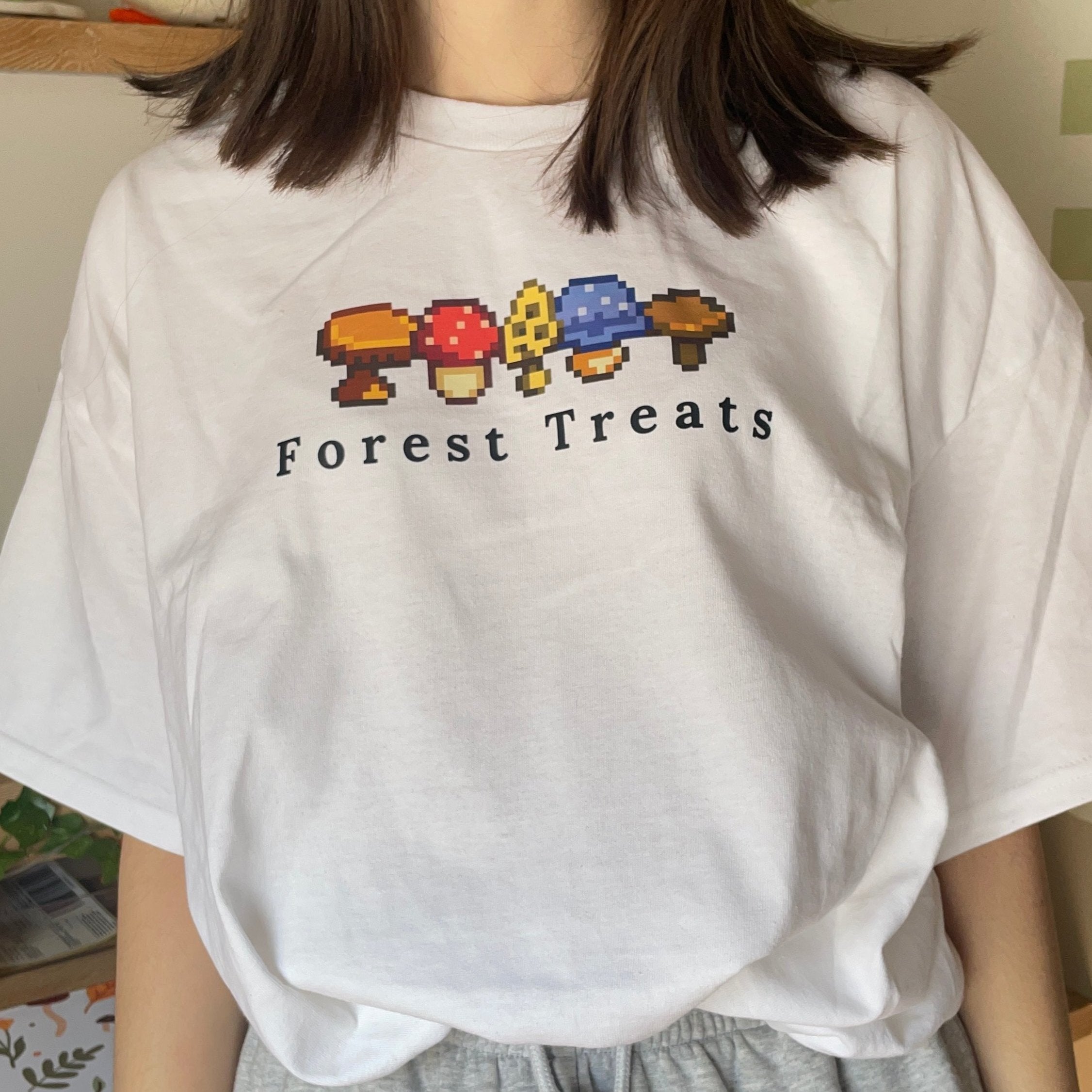 A person is dressed in a petimint Forest Treats T-Shirt, which features pixelated mushroom graphics and the text 