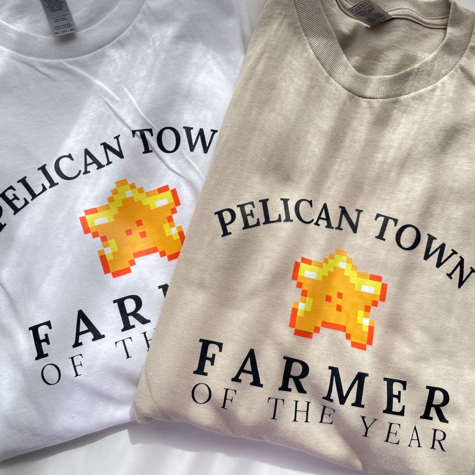 Product Data:  
  Product Name: Farmer of the Year T-Shirt
  Brand Name: petimint

Rewritten Sentence:
Two Farmer of the Year T-Shirts from petimint, one in white and the other in beige, lie side by side. Each shirt features a pixelated golden star with a smiling face and the text 