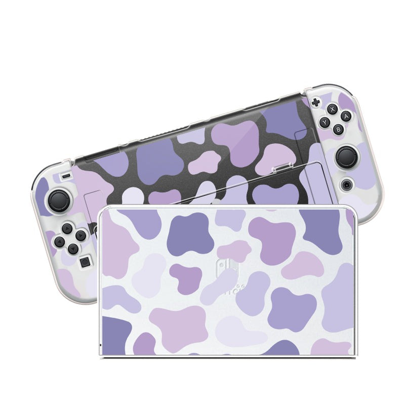 A handheld Nintendo Switch with a petimint Lilac Cow Case, featuring a light purple, dark purple, and white cow print design. The console's detachable controllers also have matching patterns. This clear case with its playful and vibrant design is perfect for cozygamers looking to add unique flair to their gaming experience.