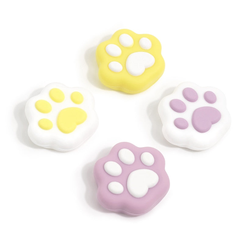 Four Yellow Cat Paw Thumb Grips for Nintendo Switch from petimint are displayed on a white background. Perfect for gamers, these grips come in pairs: two are yellow with white accents, and two are purple with white accents. Each grip features a large central pad and four smaller surrounding pads in contrasting colors.